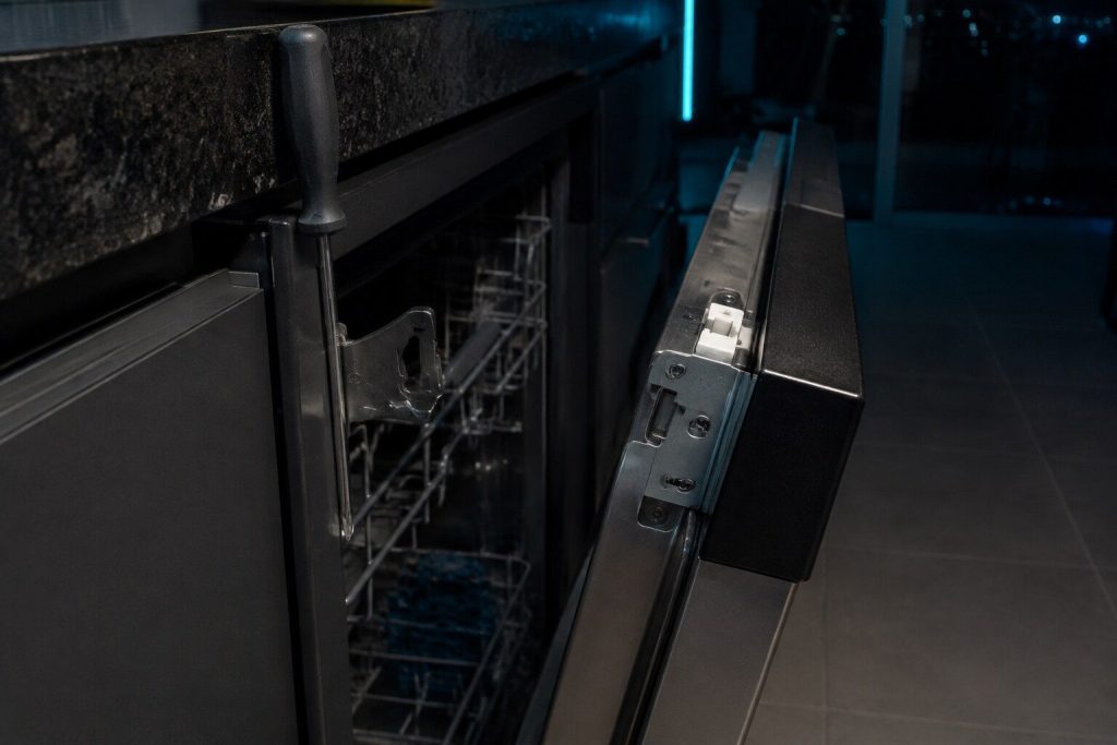 The latch at the top of a dishwasher door and the strike it closes into, the door held an inch open so both halves read.
